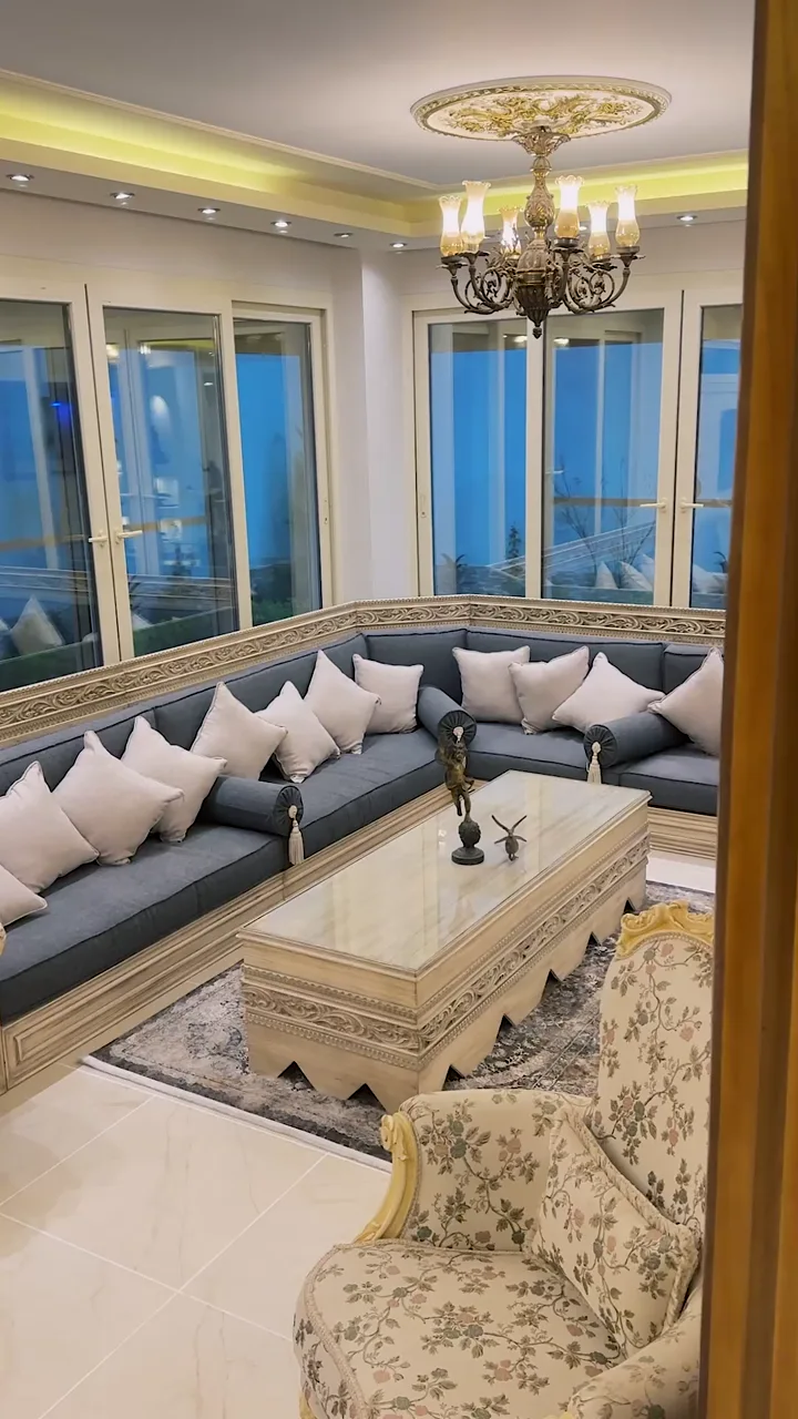 A video tour through Villa Gharb Somed, opening on its lounge with grey seating, carved furnishings and a chandelier.